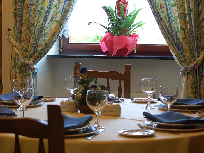 Mesa puesta junto a la ventana, con mantel amarillo, cortinas floreadas y pared de piedra.