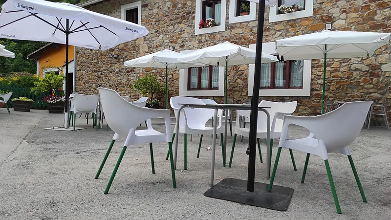 La terraza con mesas, sillas blancas y sombrillas, delante de la fachada de piedra.